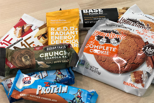 group photo of many different protein bars and protein cookies