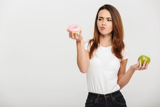 a woman holding a pink donut and and green apple deciding what to eat